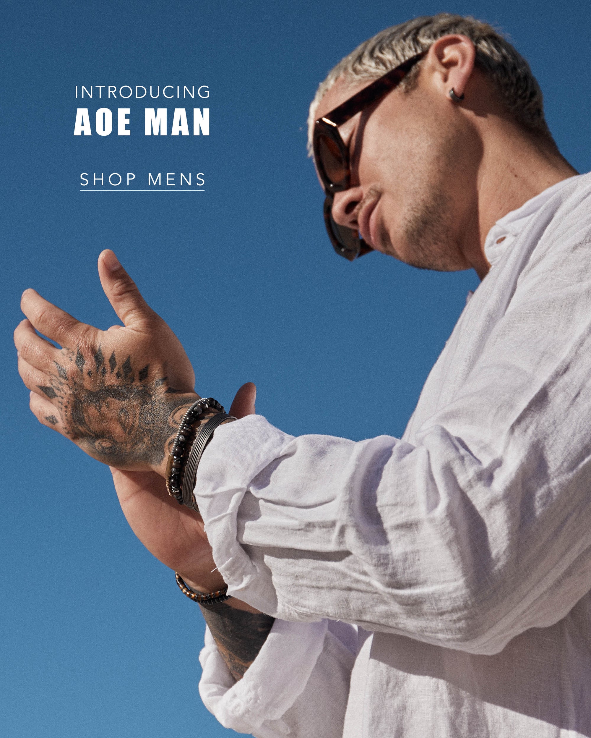 Stylish man wearing sunglasses and a white shirt, introducing the AOE Man Shop for men's jewelry and sunglasses